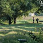 Two people walking on a green rural path in Garešnica, surrounded by trees on a sunny day.