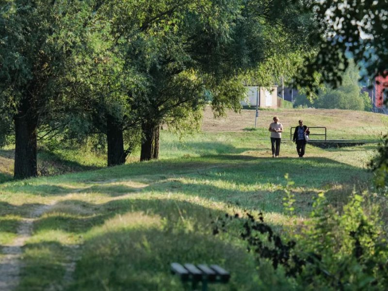 Two people walking on a green rural path in Garešnica, surrounded by trees on a sunny day.